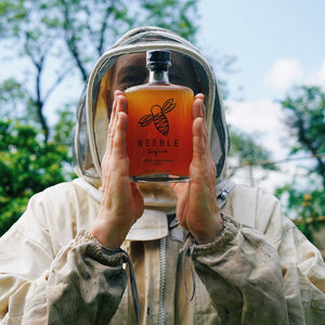 Beekeeper in protective suit holding a bottle of Beeble Original honey spirit